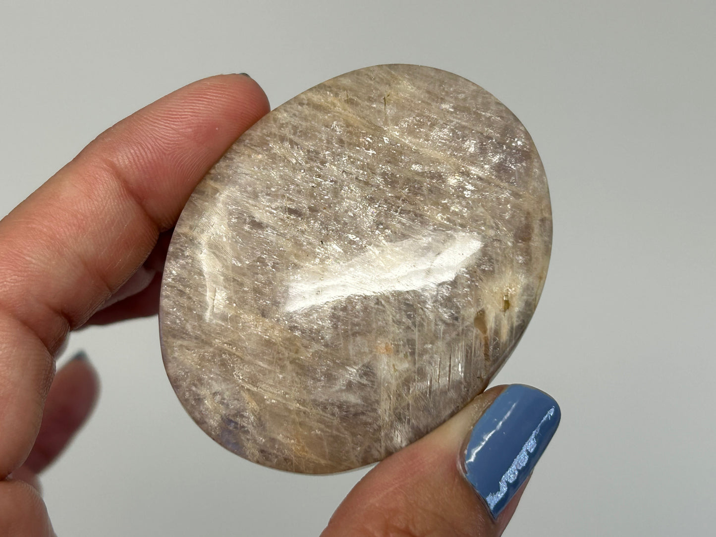 Hand holding a Blue Moonstone with Sunstone Palm Stone against a plain background