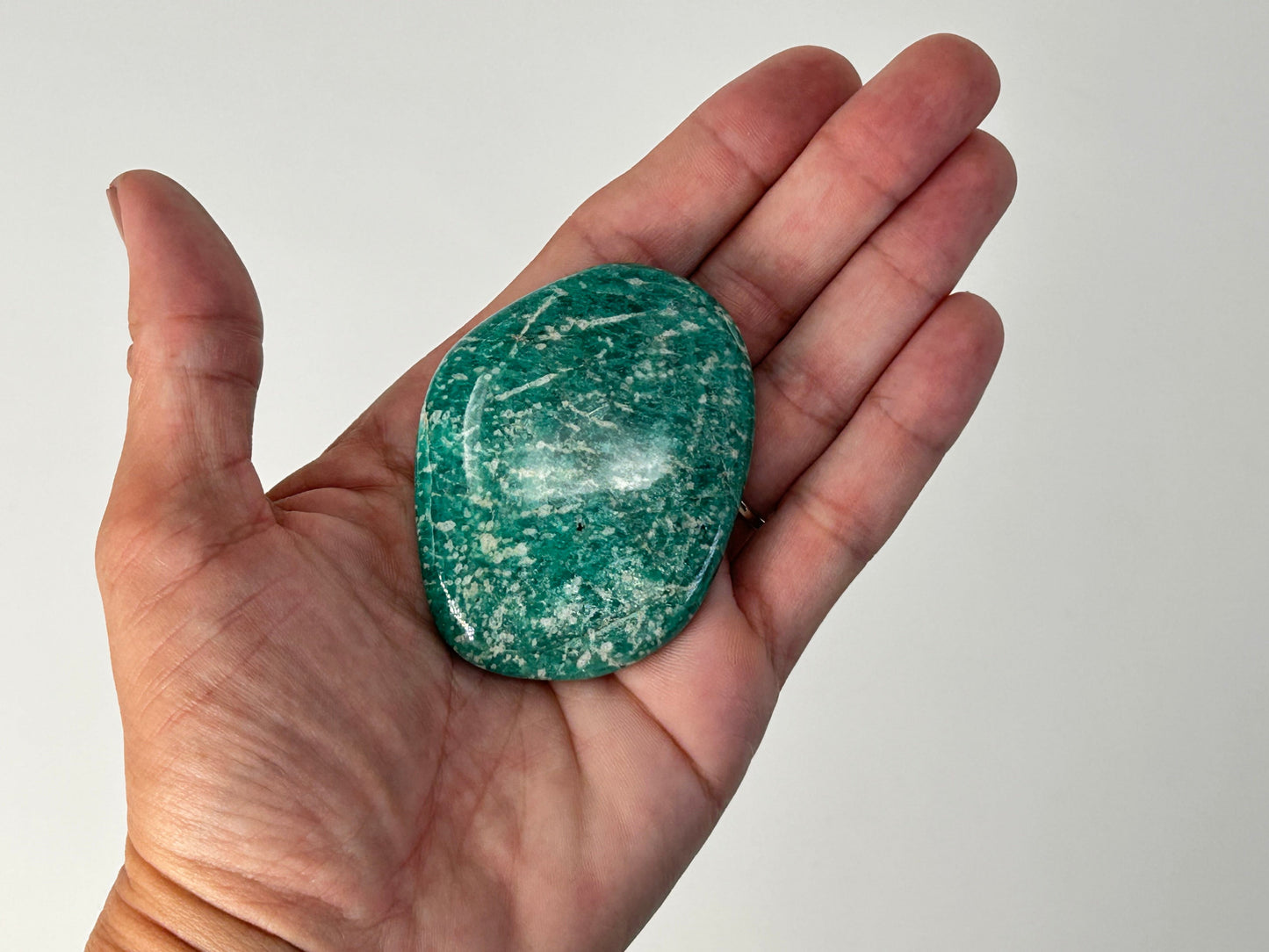 Hand holding a Energized Emerald Green Amazonite Palm Stone against a plain background