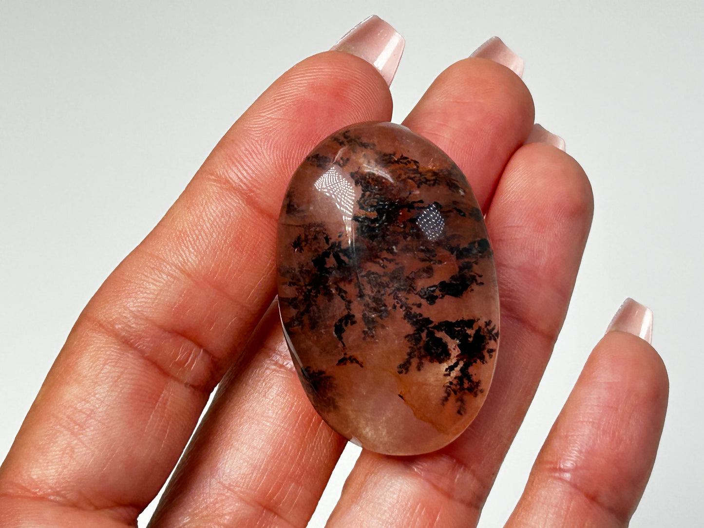 Hand holding Oval-shaped Brown Dendritic Fluorite reiki charged healing crystal with white background.