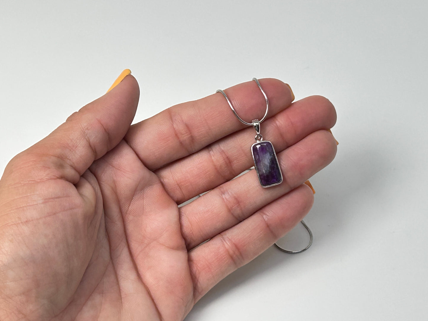 Hand holding a Purple Sugilite Crystal Pendant in Sterling Silver with white background.