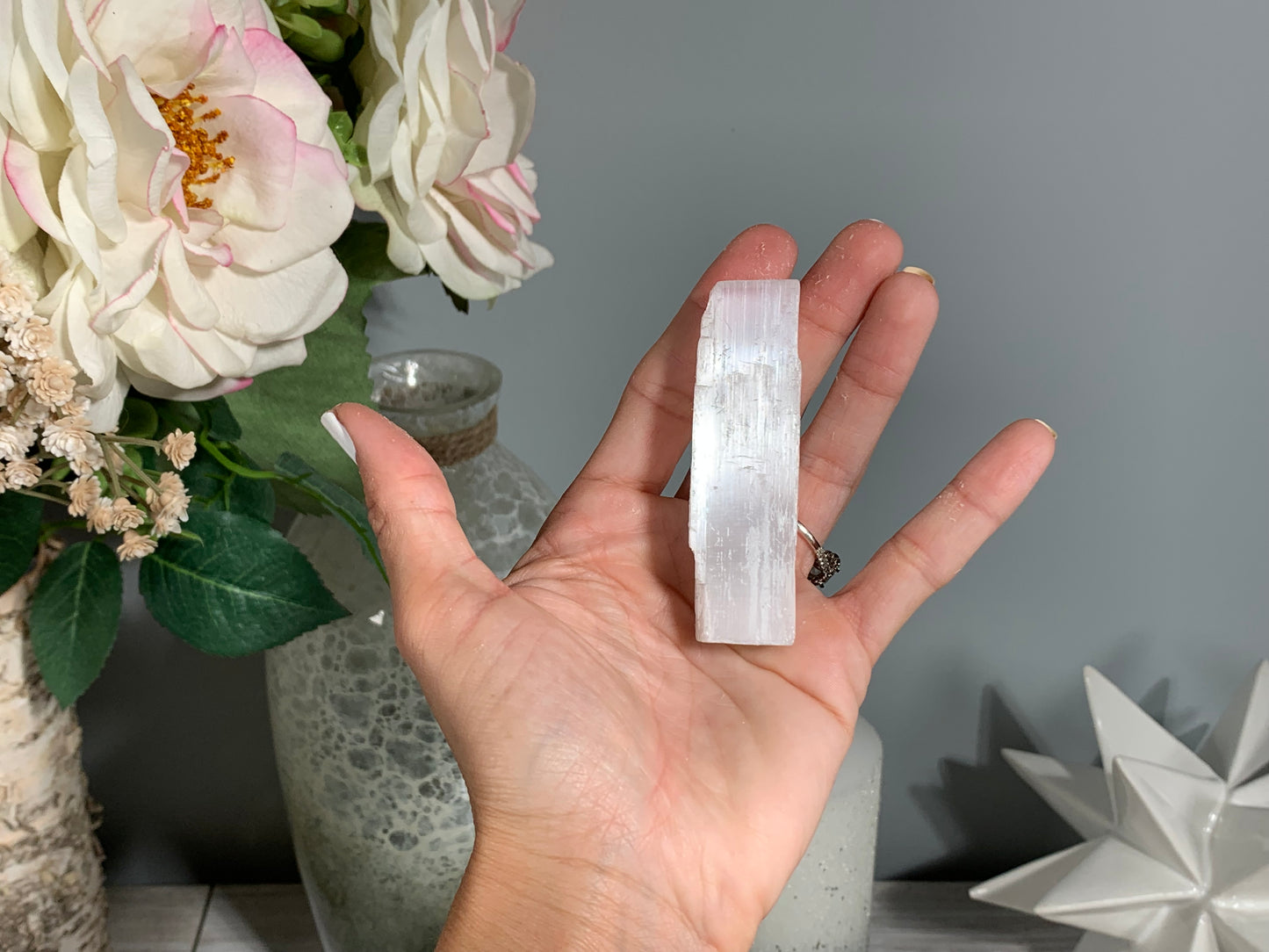 hand holding a Selenite Crystal Cleansing Stick to Purify and Protect for energy and trust with white gray floral background.