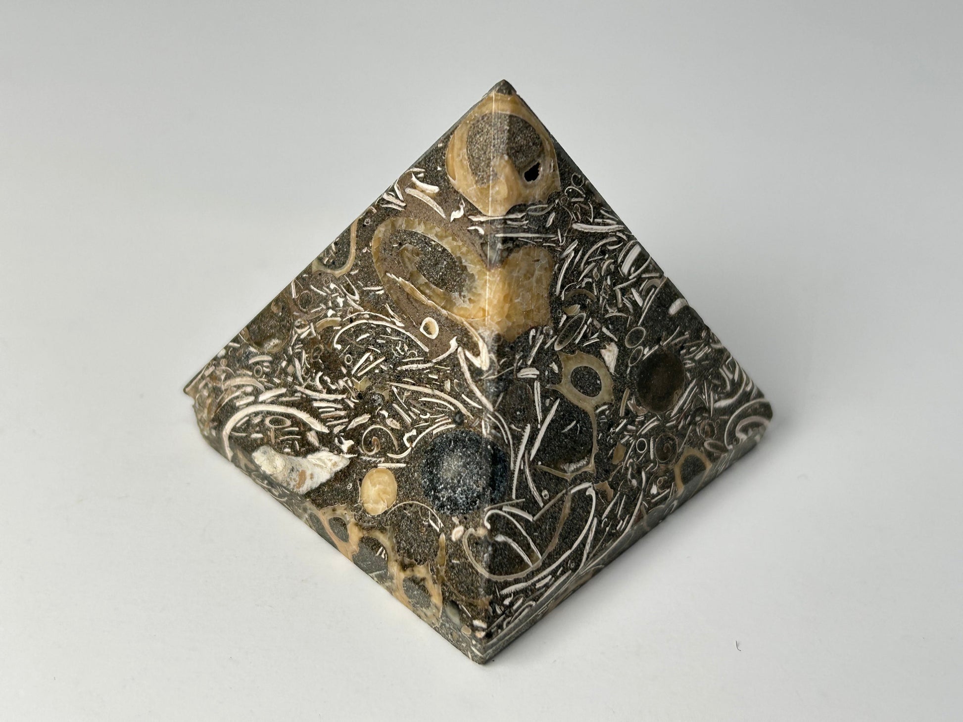 Ancient Turritella Agate Pyramid with intricate carvings on a gray background