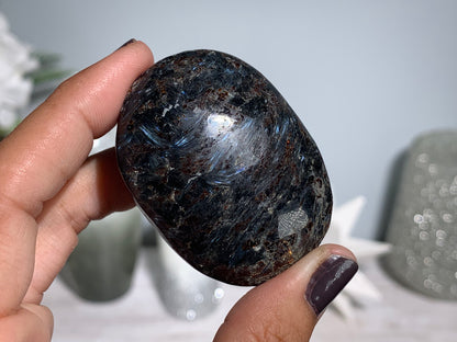 hand holding a Anthophyllite in Eudialyte with Pyrite Palm Stone Crystal against a white gray floral background