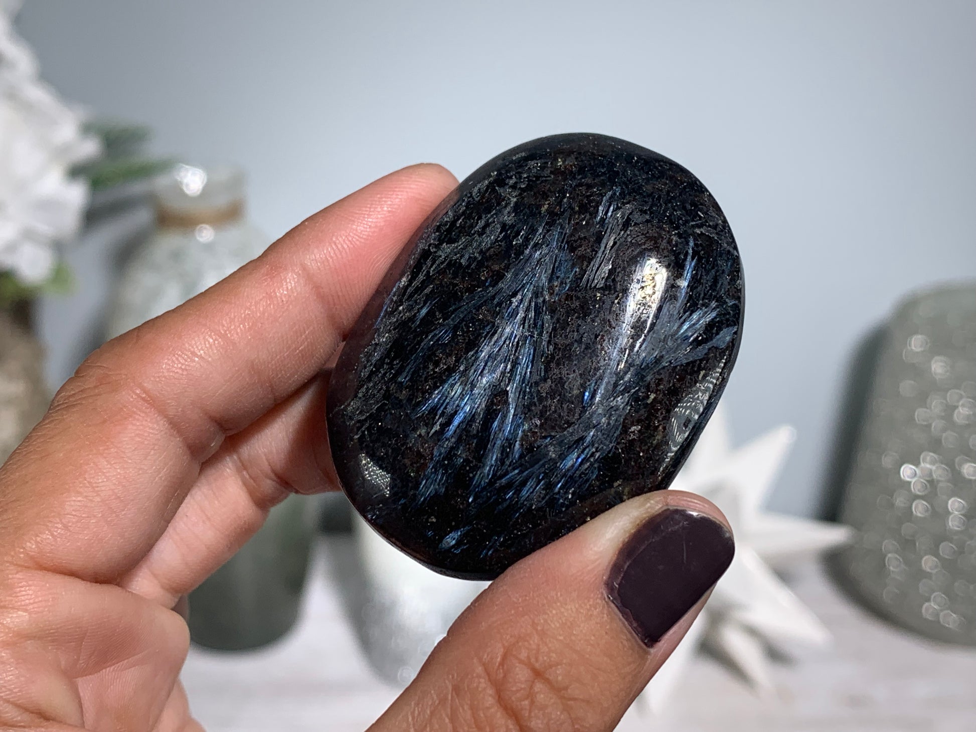 hand holding a Anthophyllite in Eudialyte with Pyrite Palm Stone Crystal against a white gray floral background