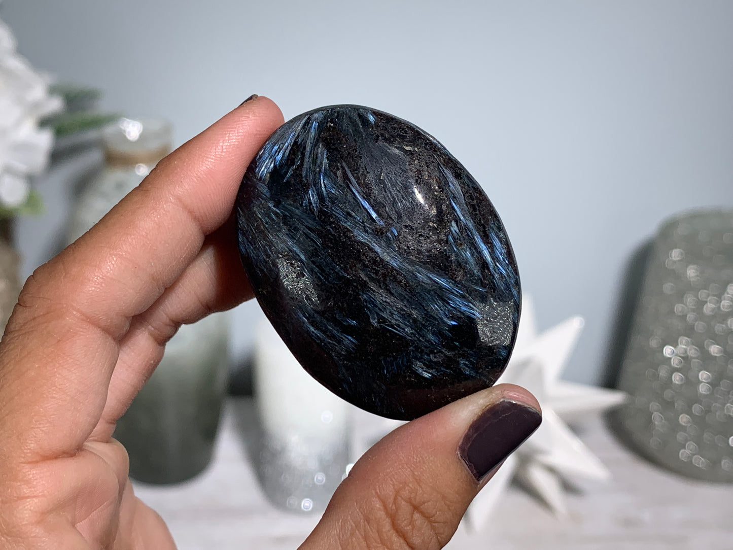 hand holding a Anthophyllite in Eudialyte with Pyrite Palm Stone Crystal against a white gray floral background