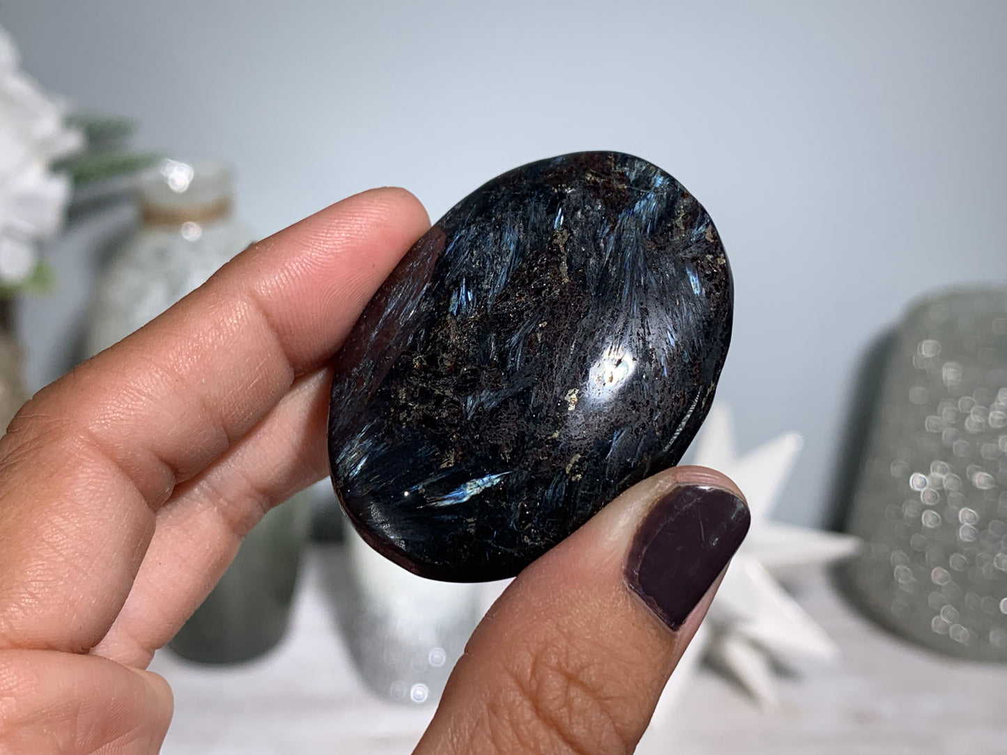 hand holding a Anthophyllite in Eudialyte with Pyrite Palm Stone Crystal against a white gray floral background