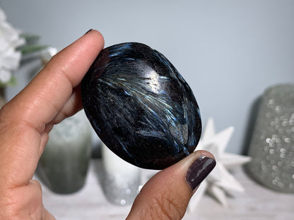 hand holding a Anthophyllite in Eudialyte with Pyrite Palm Stone Crystal against a white gray floral background