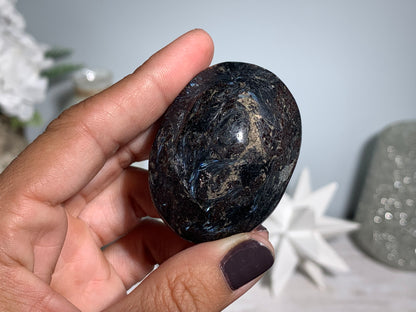 hand holding a Anthophyllite in Eudialyte with Pyrite Palm Stone Crystal against a white gray floral background