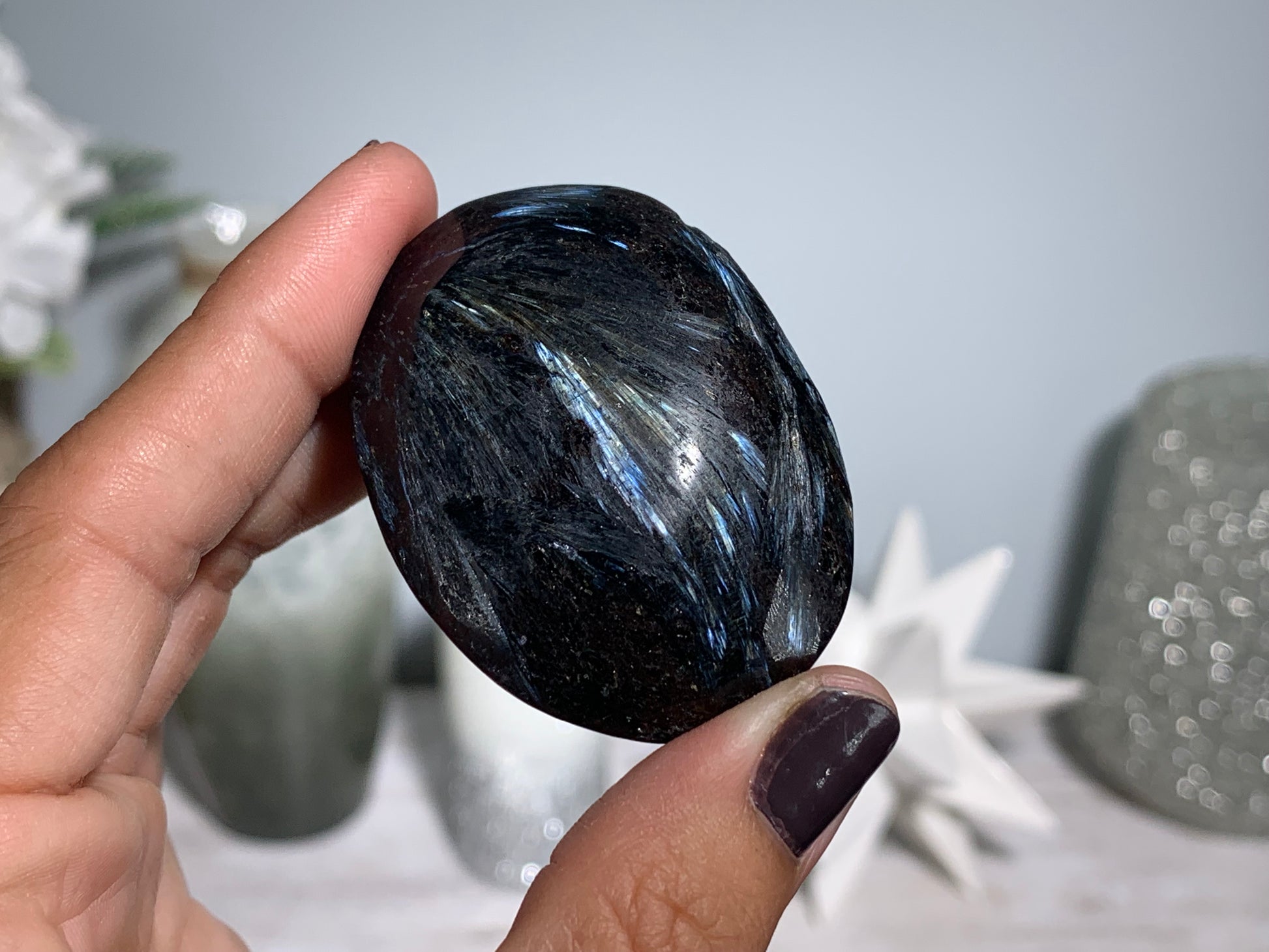 hand holding a Anthophyllite in Eudialyte with Pyrite Palm Stone Crystal against a white gray floral background