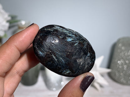 hand holding a Anthophyllite in Eudialyte with Pyrite Palm Stone Crystal against a white gray floral background