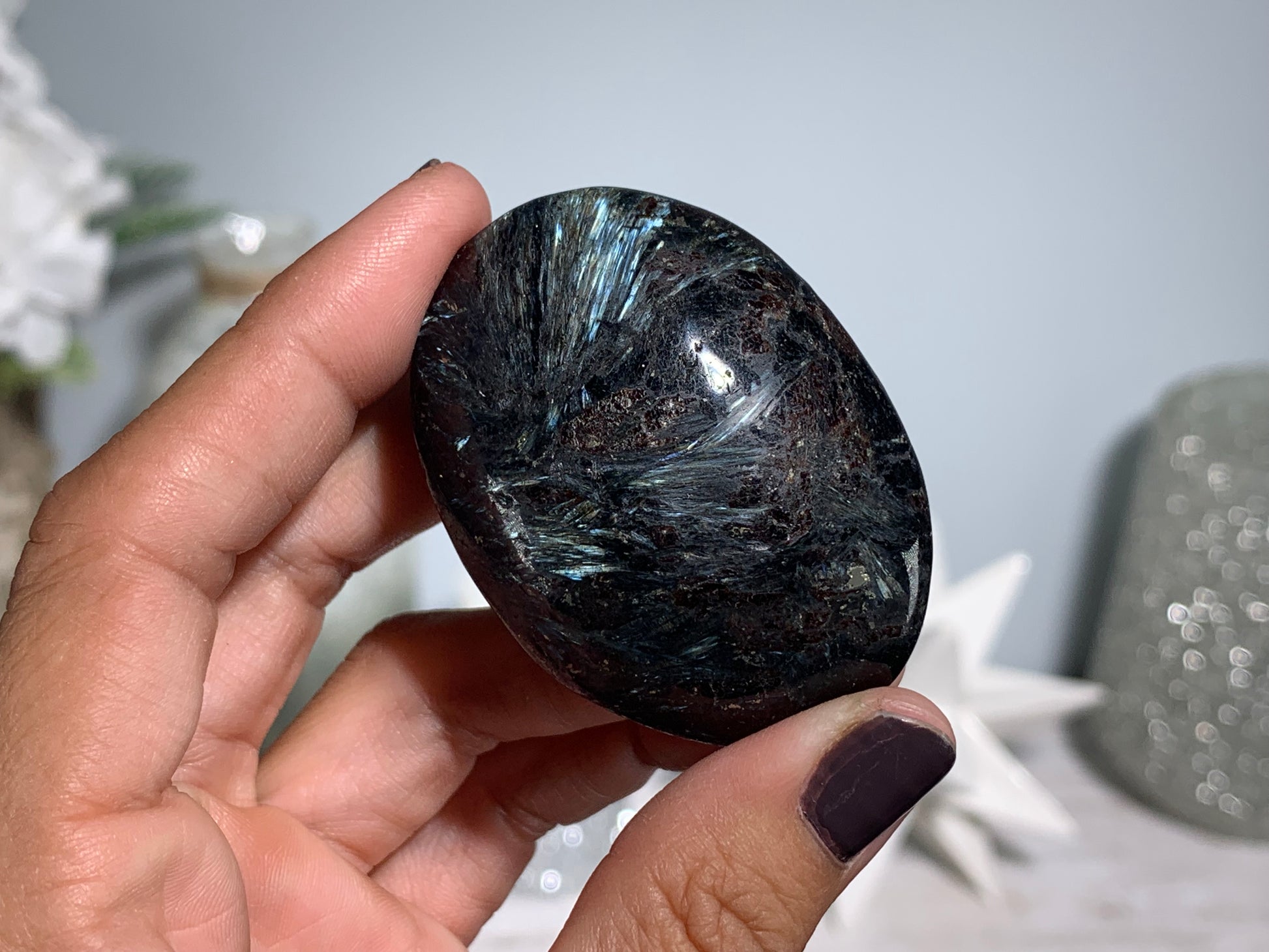 hand holding a Anthophyllite in Eudialyte with Pyrite Palm Stone Crystal against a white gray floral background