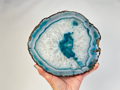 Hand holding an Aqua Blue Agate Geode Slice with gold trim for spiritual healing against white background