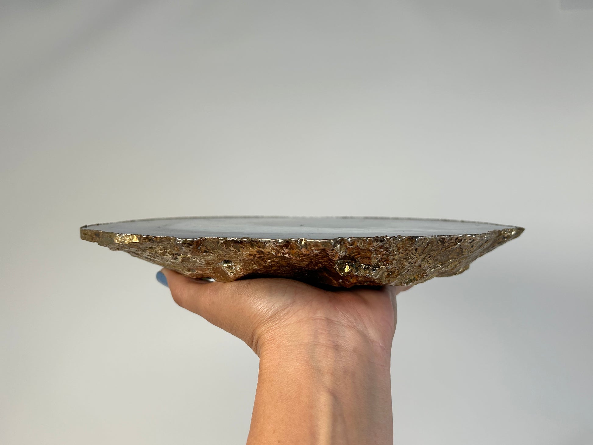 Hand holding a Blue Agate Stone Plate with gold trim on a plain background