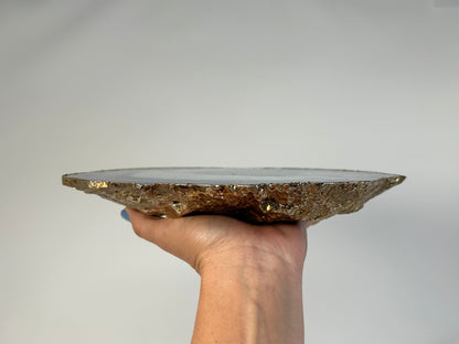 Hand holding a Blue Agate Stone Plate with gold trim on a plain background