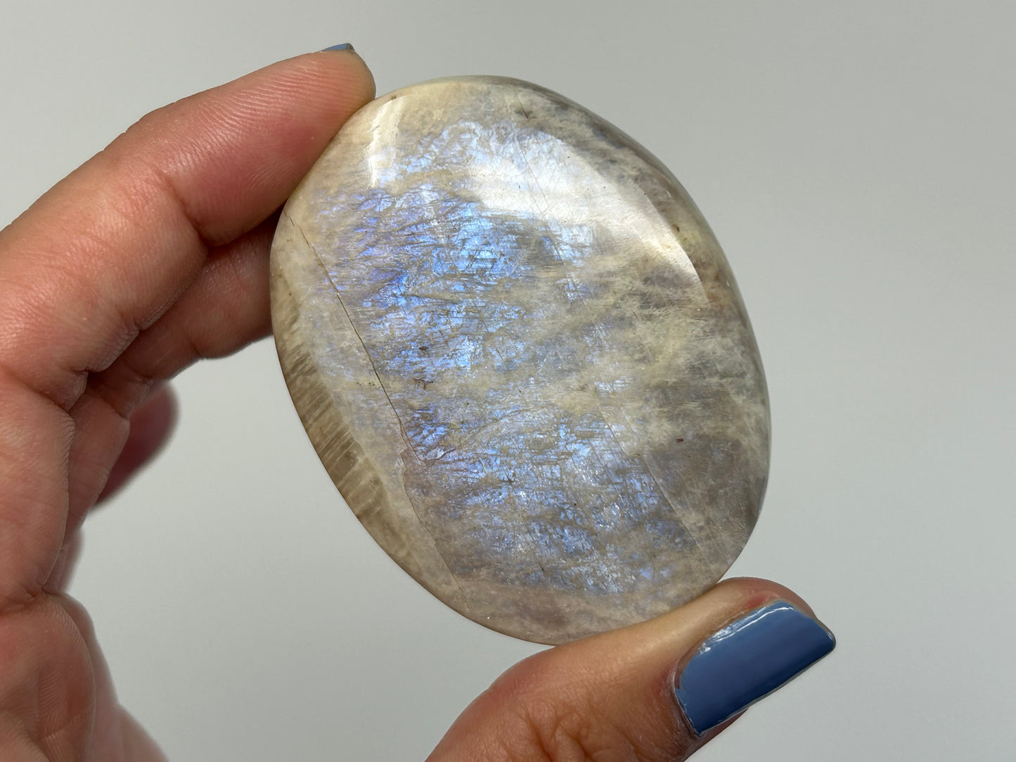 Hand holding a polished Blue Moonstone with Sunstone Palm Stone against a plain background
