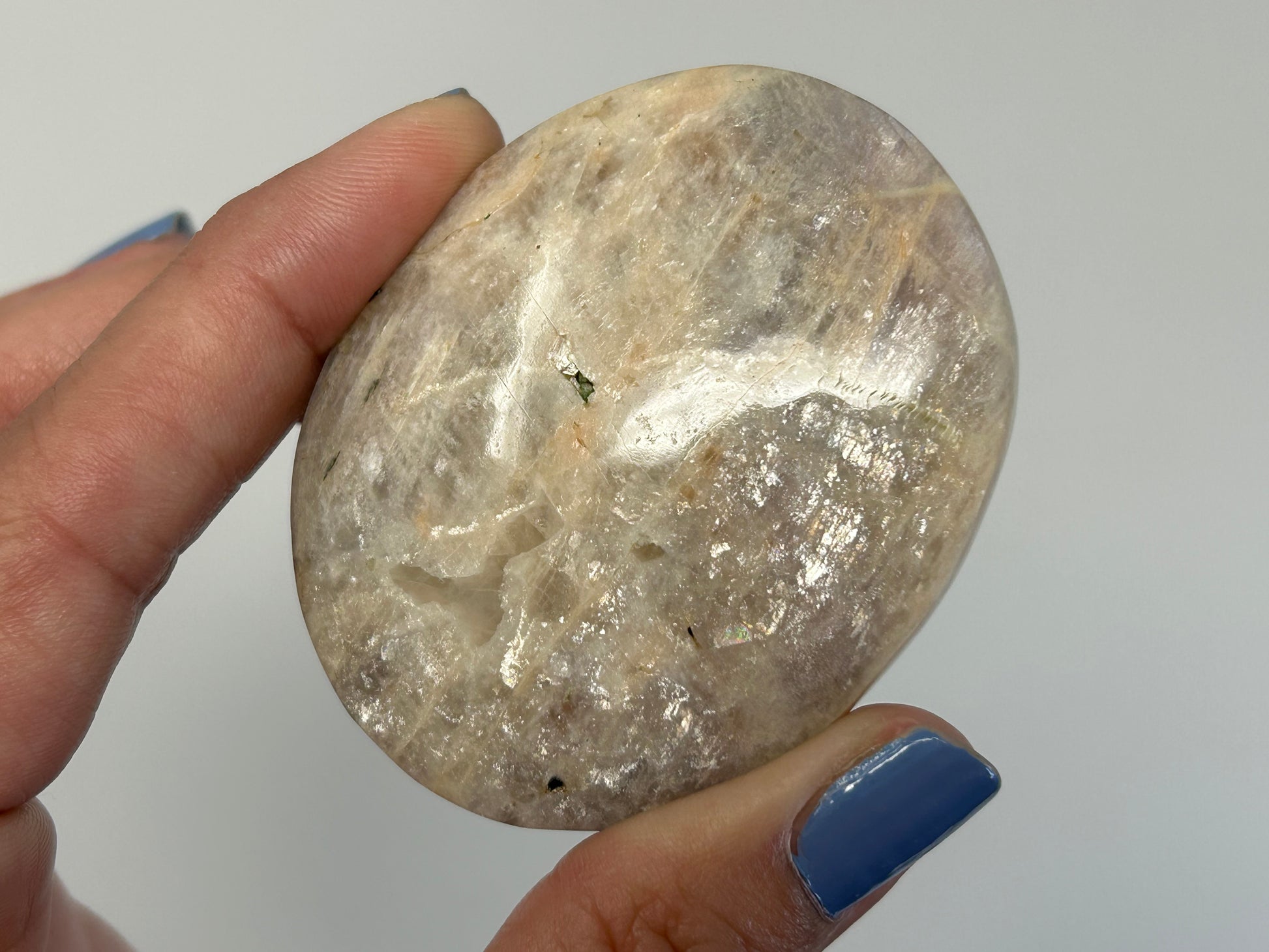 Hand holding a Blue Moonstone with Sunstone Palm Stone for meditation and energy work with white background.