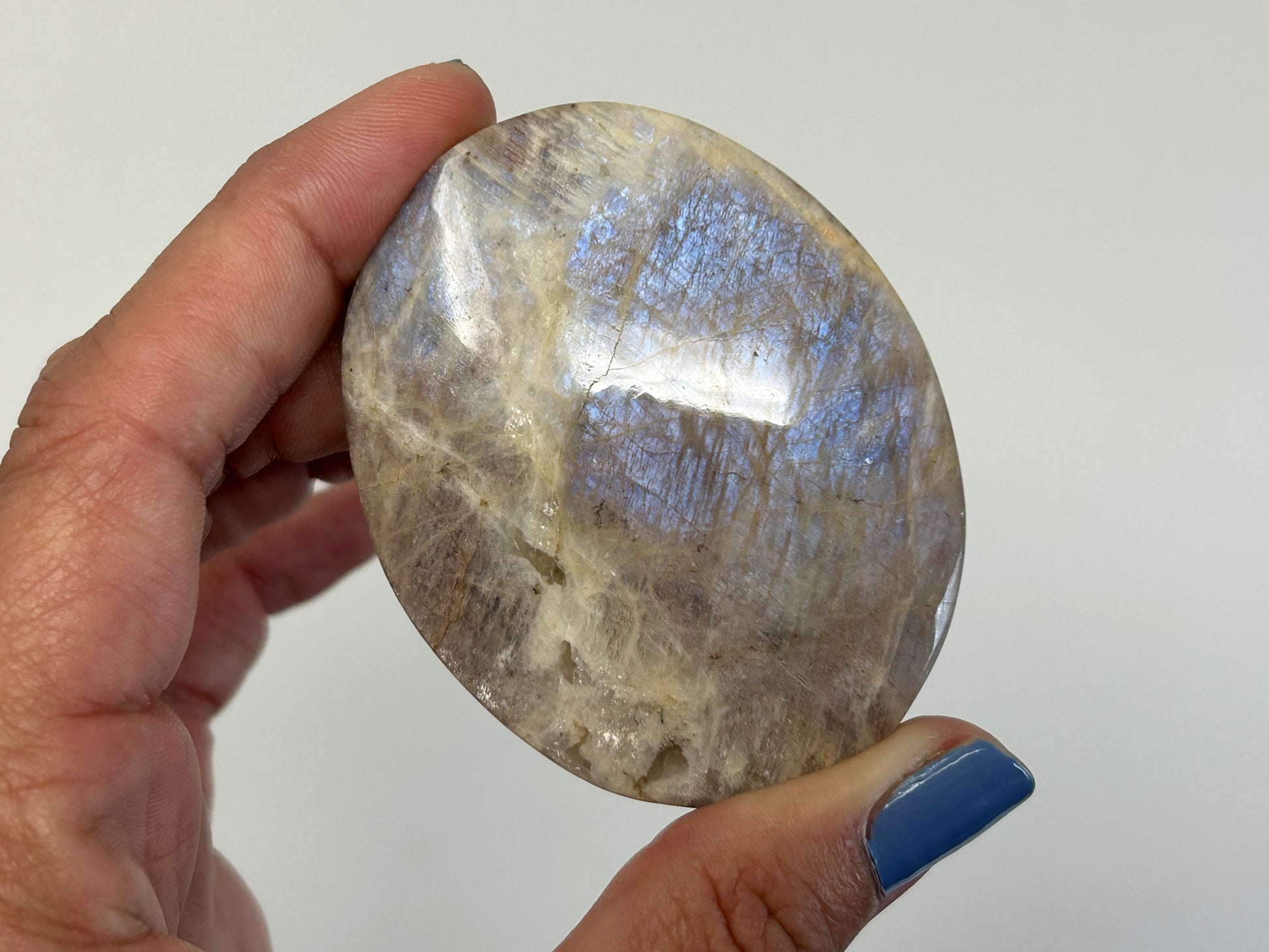 Hand holding a Blue Moonstone with Sunstone Palm Stone for spiritual healing against white background.