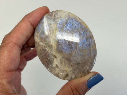 Hand holding a Blue Moonstone with Sunstone Palm Stone for spiritual healing against white background.