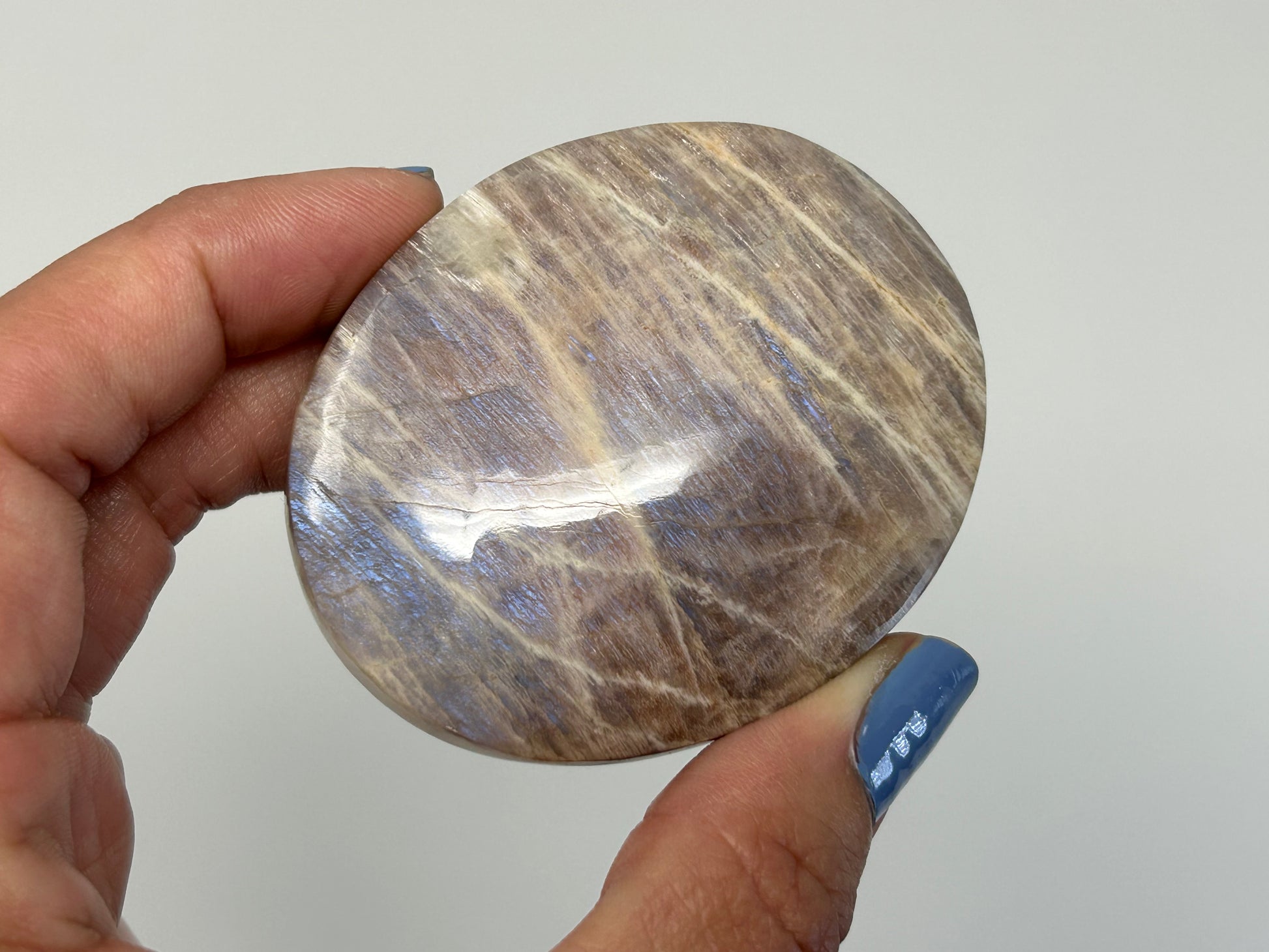 Hand holding an ethically sourced Blue Moonstone with Sunstone Palm Stone for meditation over white background.