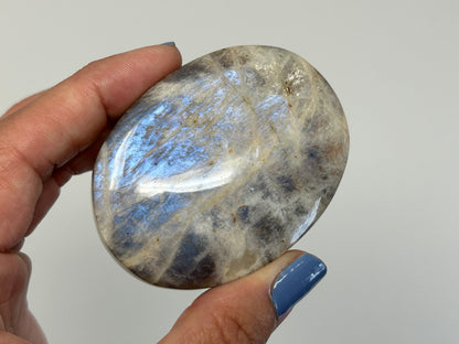 Hand holding a polished Blue Moonstone with Sunstone Palm Stone against a plain background