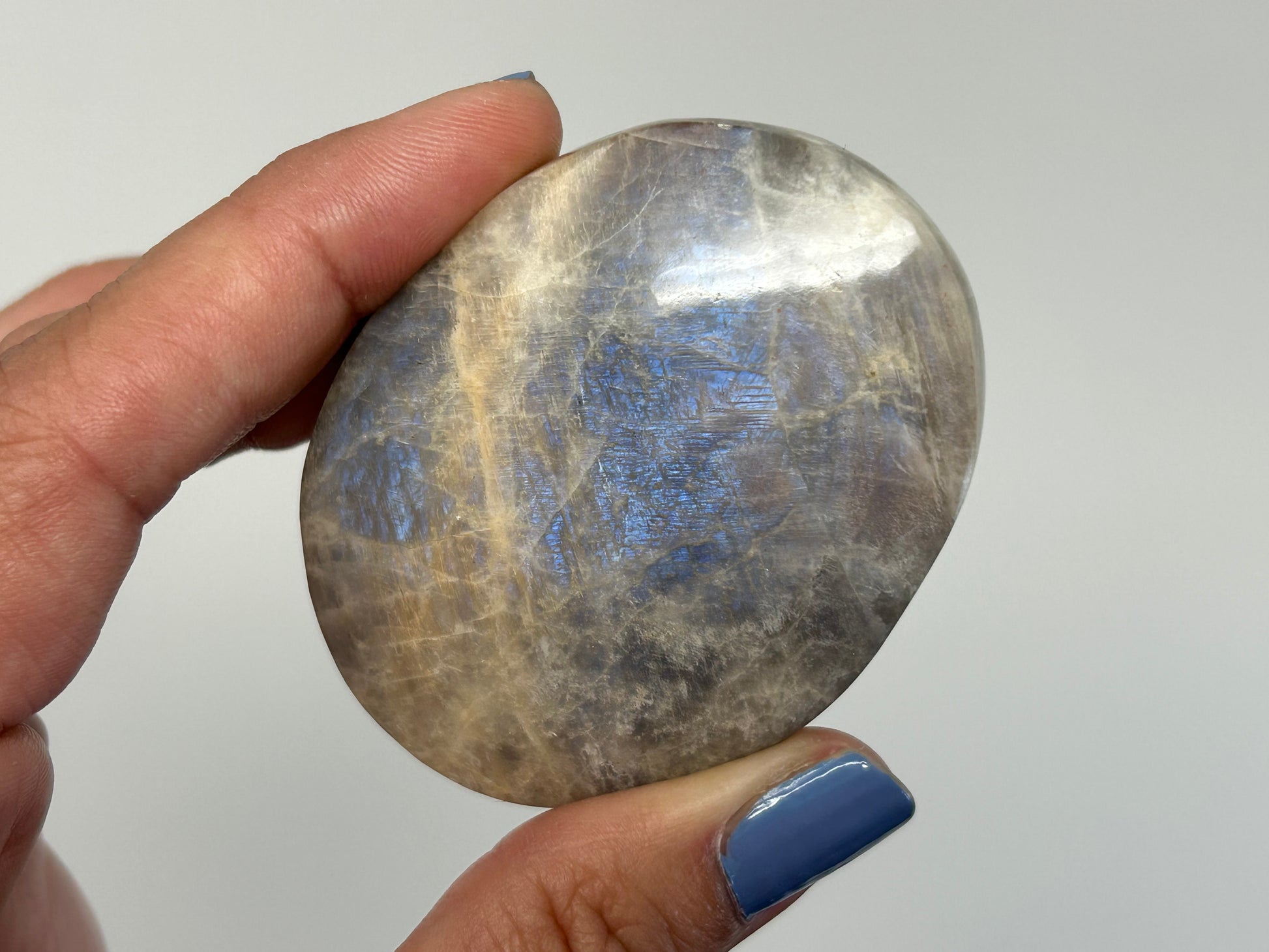 Hand holding a polished Blue Moonstone with Sunstone Palm Stone against a neutral background