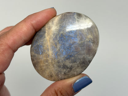 Hand holding a polished Blue Moonstone with Sunstone Palm Stone against a neutral background