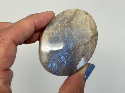 Hand holding Blue Moonstone with Sunstone Palm Stone with white background.
