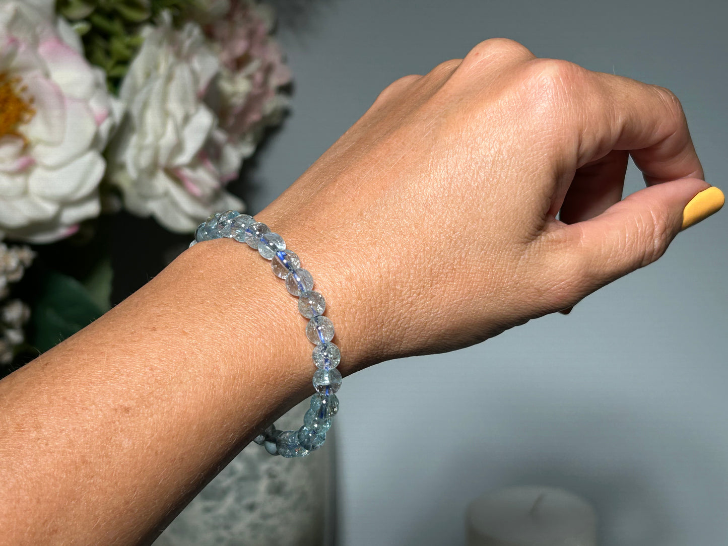 Hand wearing a Blue Topaz Bracelet for meditation, mindfulness and grounding with flowers and a candle in the background