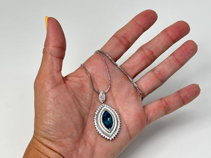 Hand holding a silver necklace with a Blue Topaz Eye Pendant with Cubic Zirconia in Sterling Silver for meditation and energy work with white gray floral background