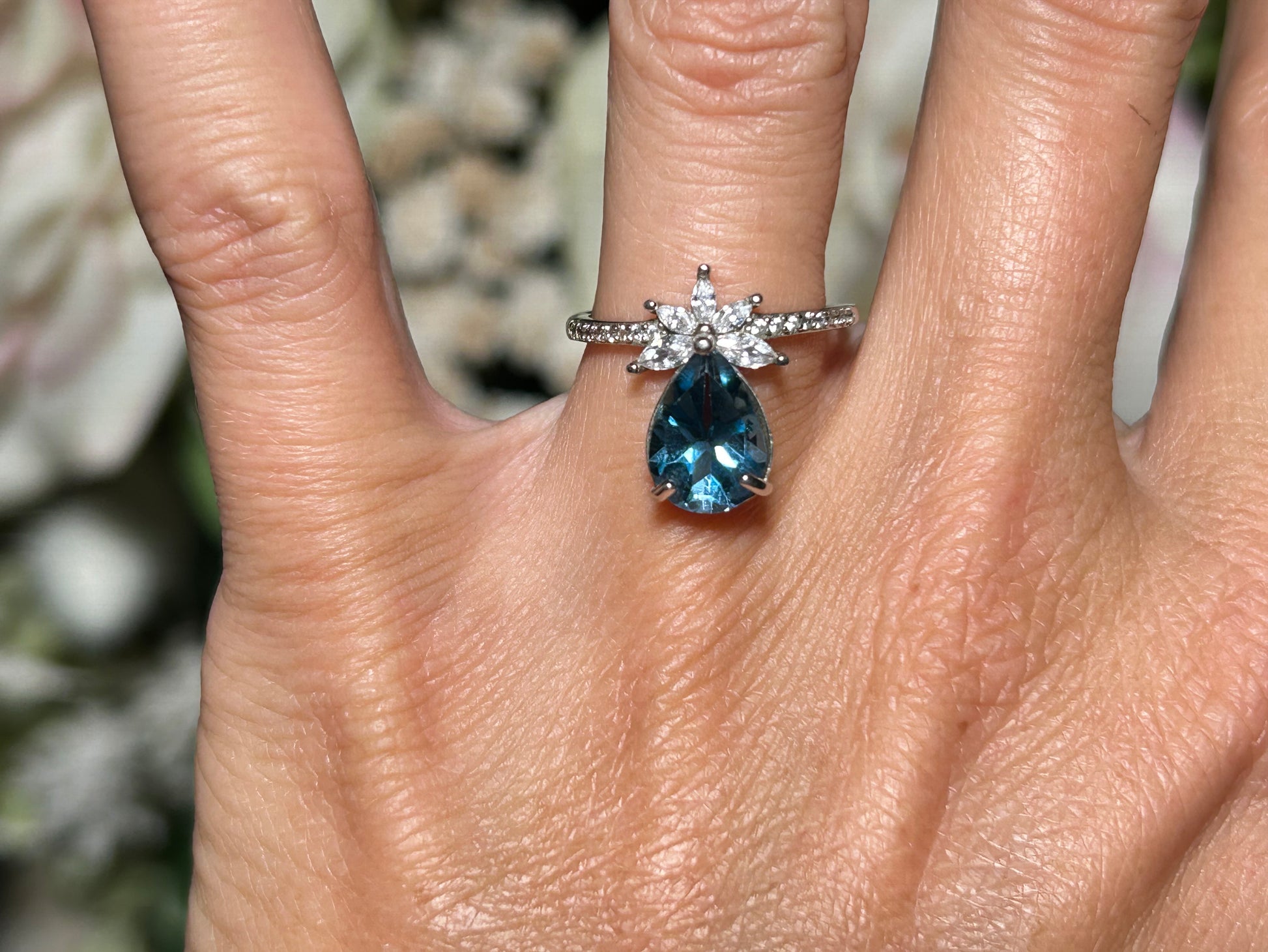Close-up of a hand wearing a Blue Topaz Ring with Cubic Zirconia in Sterling Silver on a blurred background