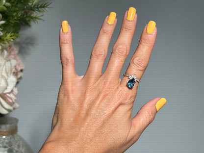 Hand wearing a Blue Topaz Ring with Cubic Zirconia in Sterling Silver for spiritual healing against gray floral background