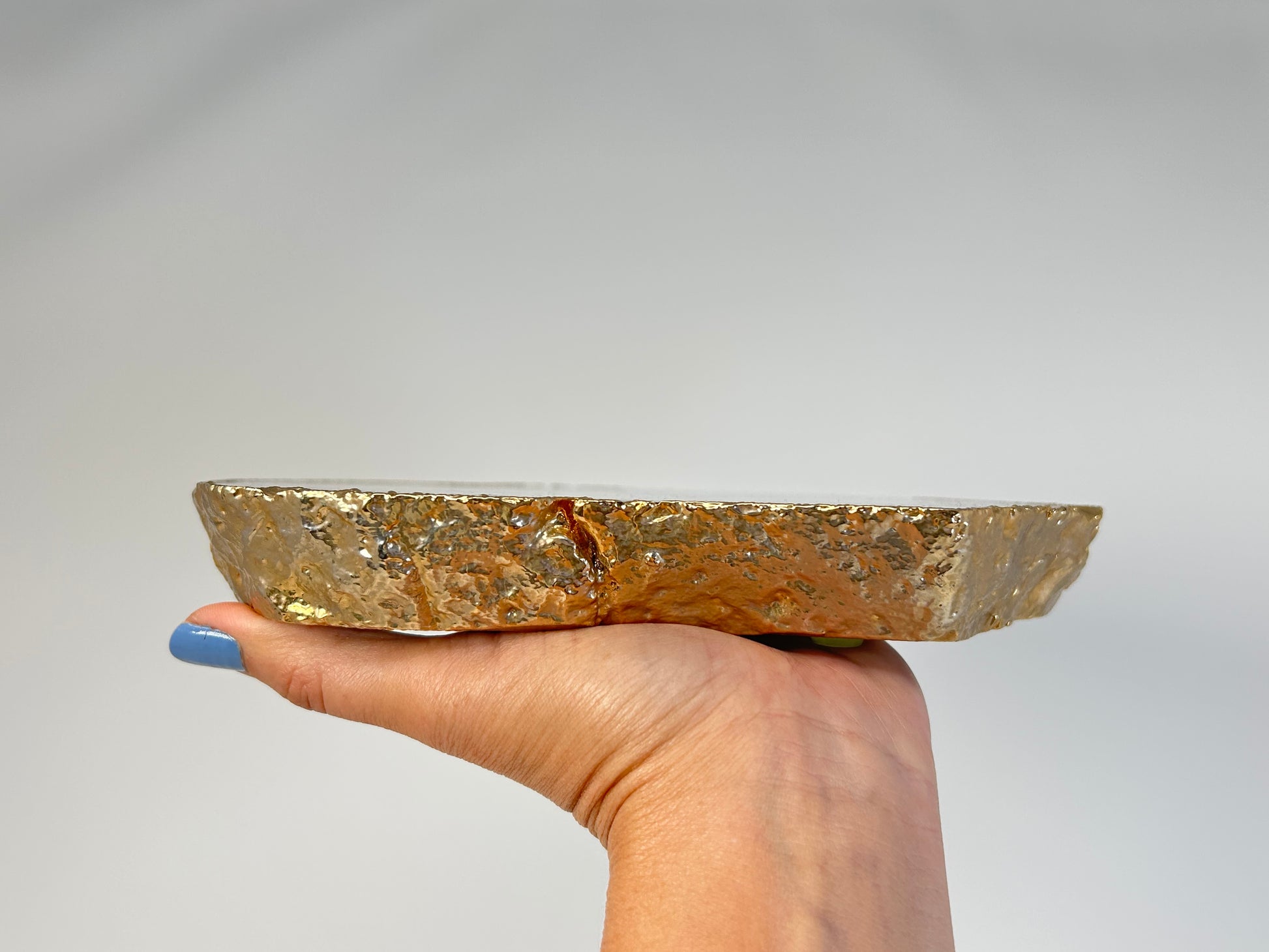 Hand holding a Calming and harmonizing Dyed Blue Agate Plate for spiritual healing against white background