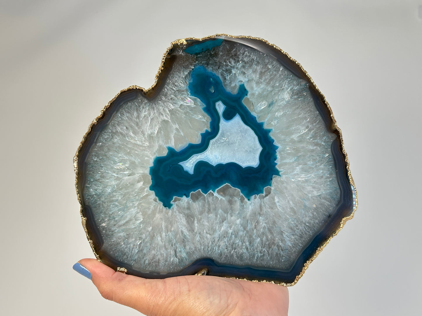 Hand holding a Calming and harmonizing Dyed Blue Agate Plate for meditation and energy work with white background