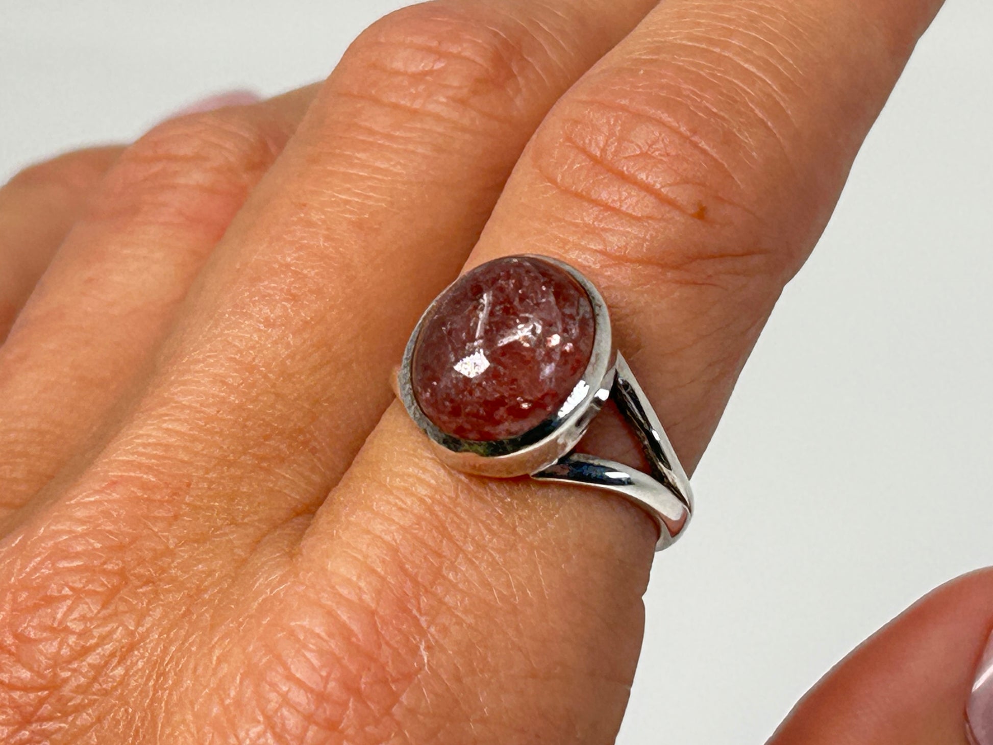 Hand wearing a Cherry Tanzurine Sterling Silver Ring for spiritual healing against white background.