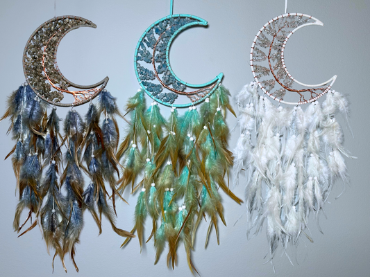 Three moon-shaped dream catchers with feathers on a light gray background