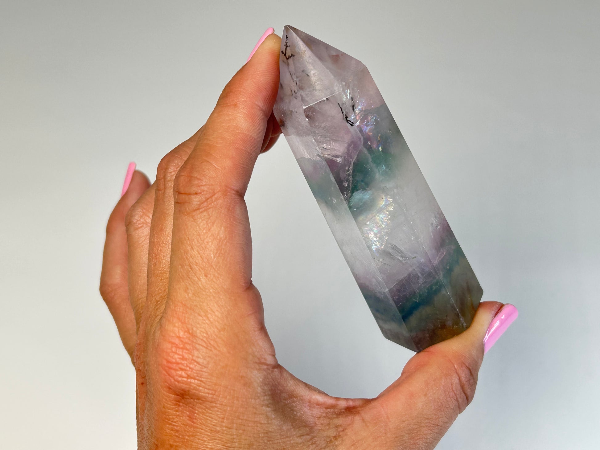Hand holding a Dendritic Fluorite Tower gemstone on table top with white background