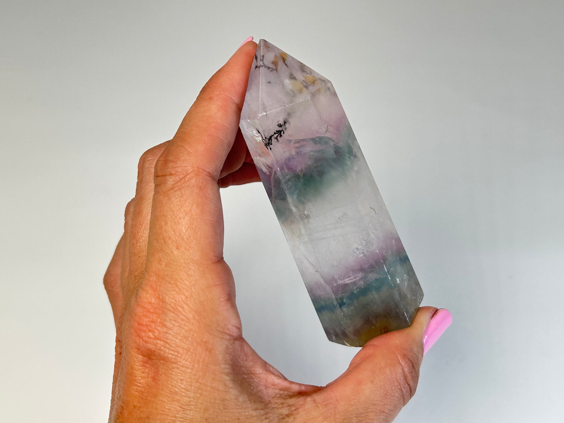 Hand holding a Dendritic Fluorite Tower gemstone on table top with white background
