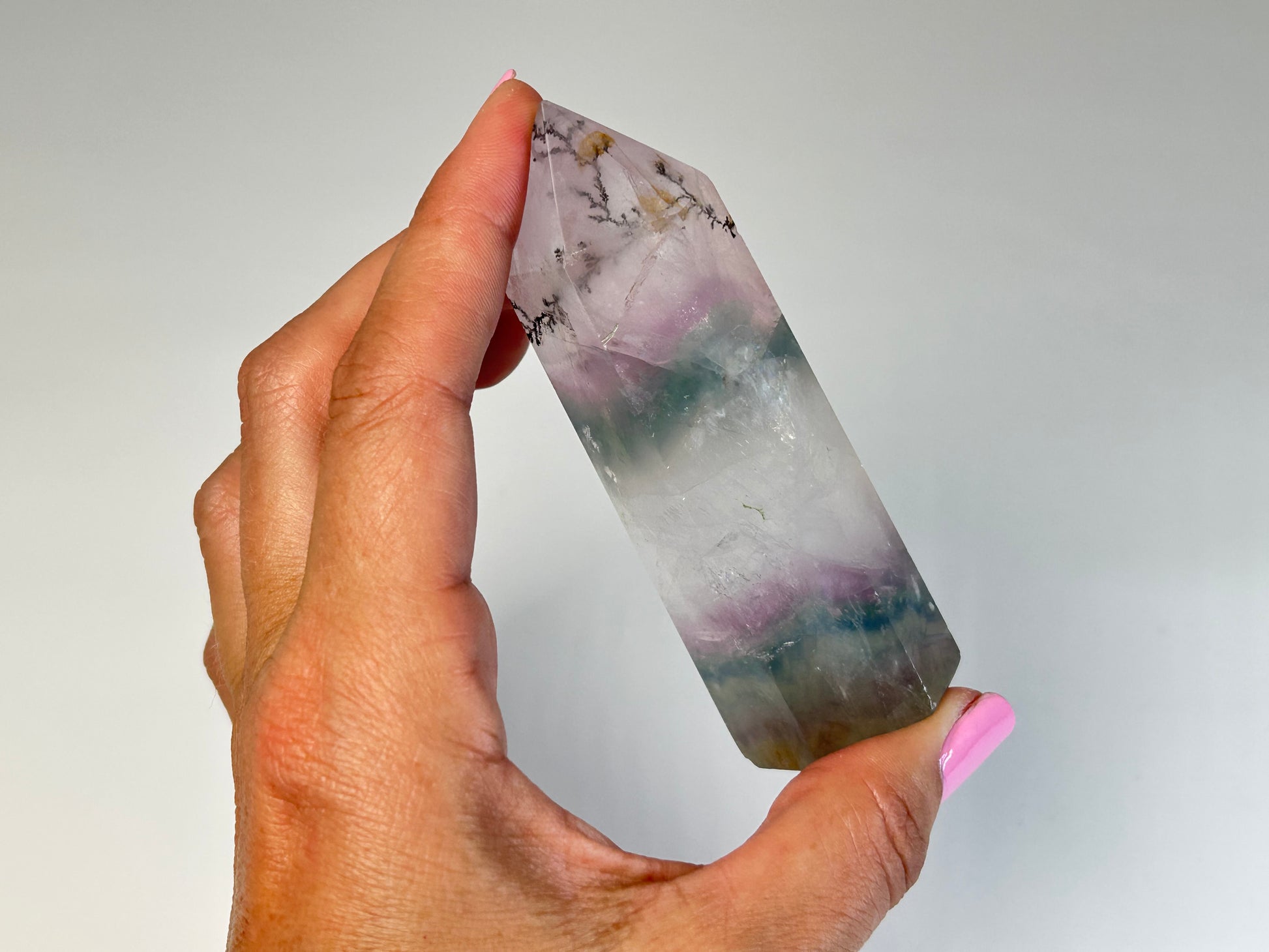 Hand holding a Dendritic Fluorite Tower gemstone on table top with white background
