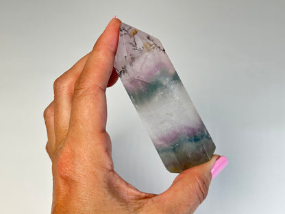 Hand holding a Dendritic Fluorite Tower gemstone on table top with white background