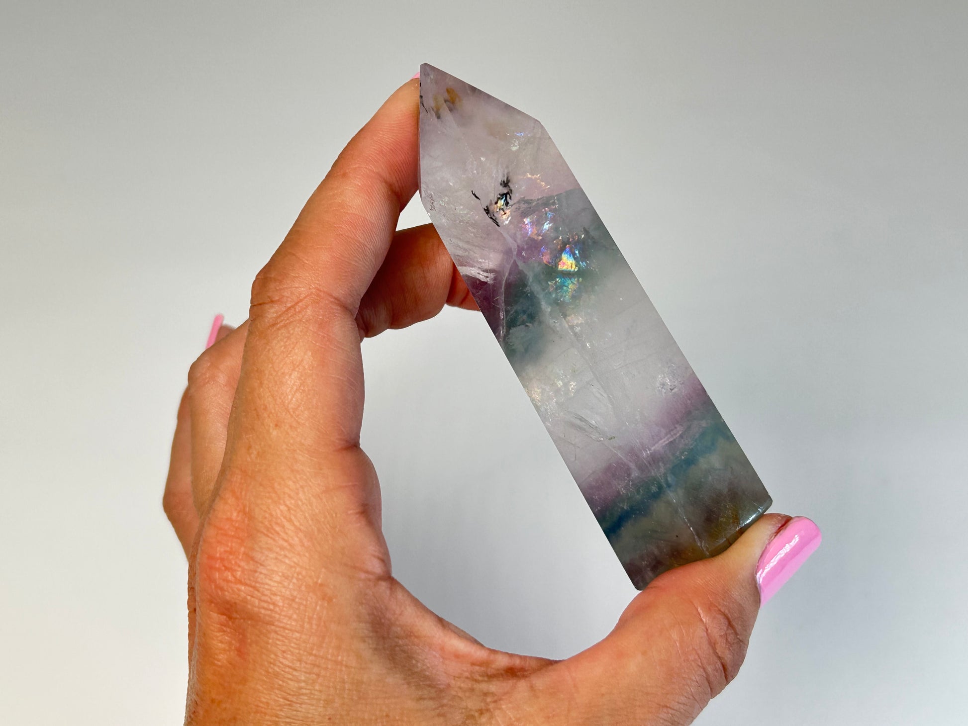 Hand holding a Dendritic Fluorite Tower gemstone on table top with white background