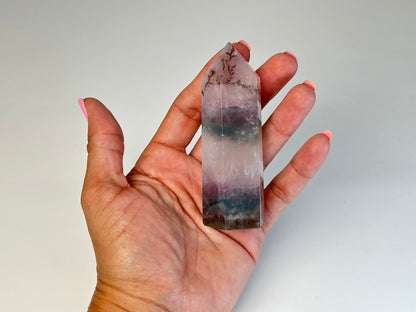 Hand holding a Dendritic Fluorite Tower gemstone with white background.
