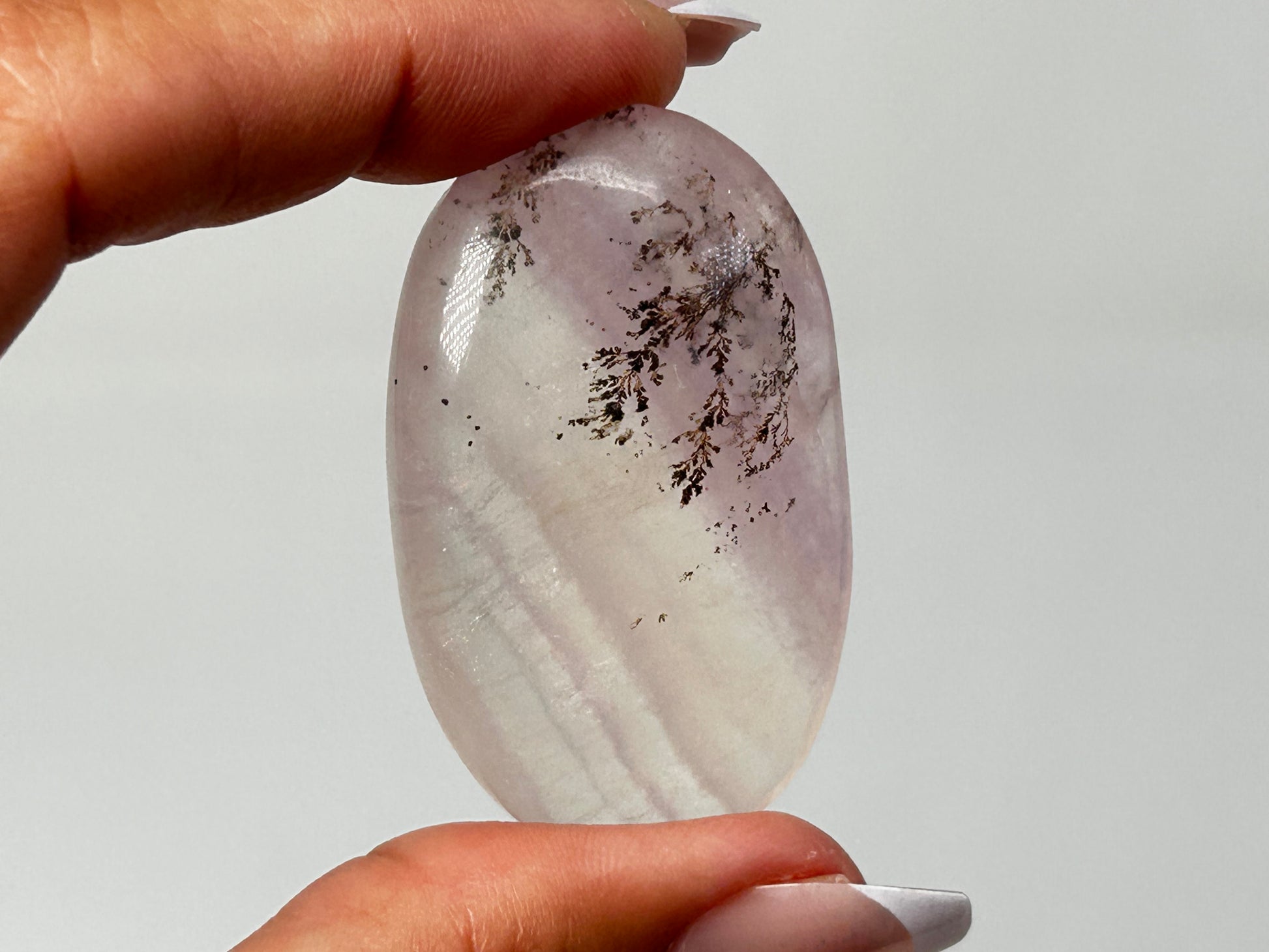 Hand holding beautiful Oval-shaped Dendritic Fluorite a beautiful ethically sourced natural healing crystal gemstone for meditation over white background.