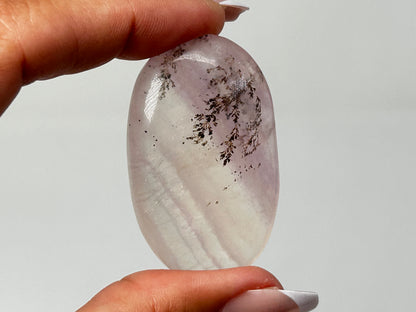 Hand holding beautiful Oval-shaped Dendritic Fluorite a beautiful ethically sourced natural healing crystal gemstone for meditation over white background.