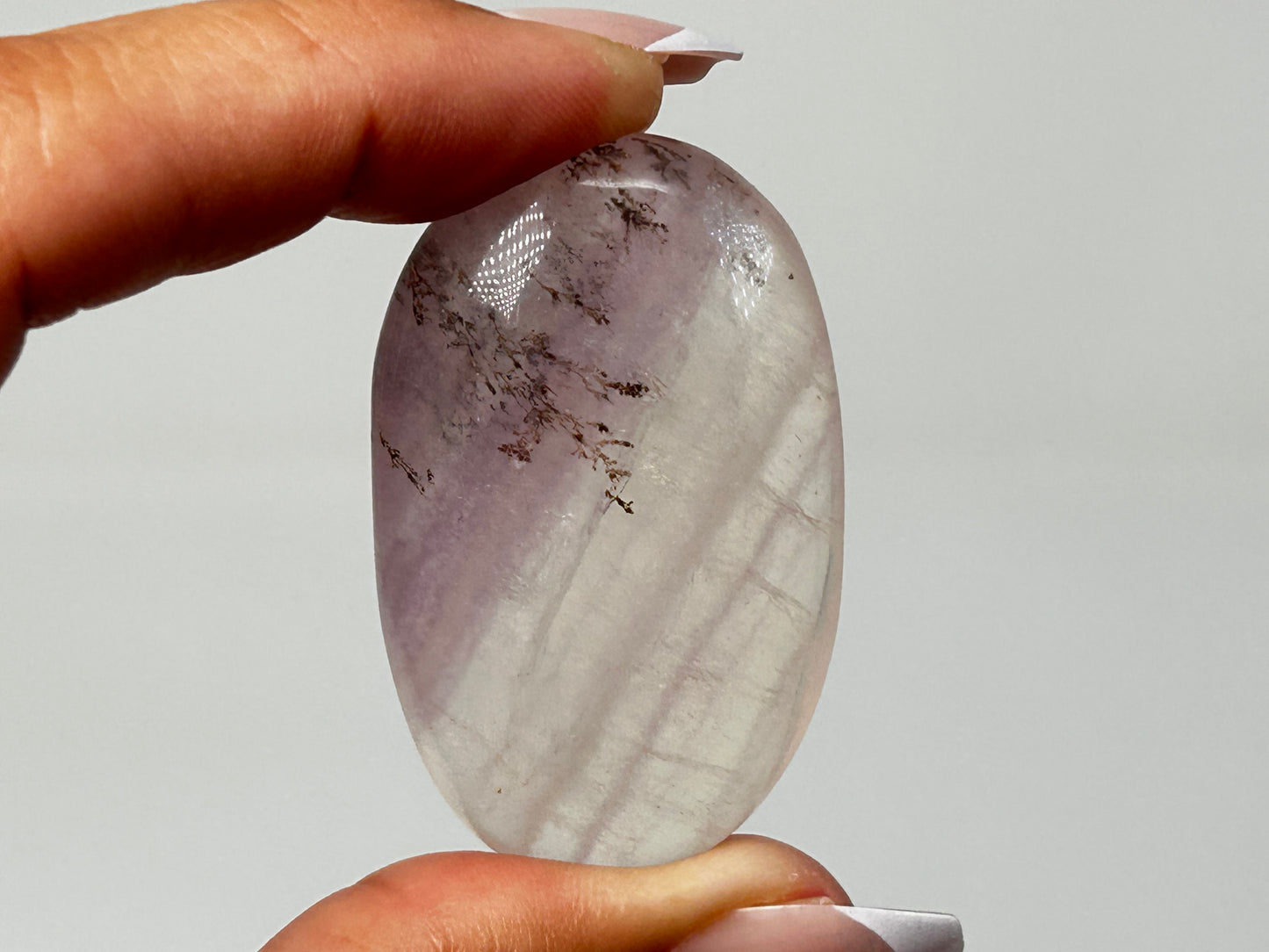 Hand holding oval-shaped Dendritic Fluorite reiki charged healing crystal with white background.
