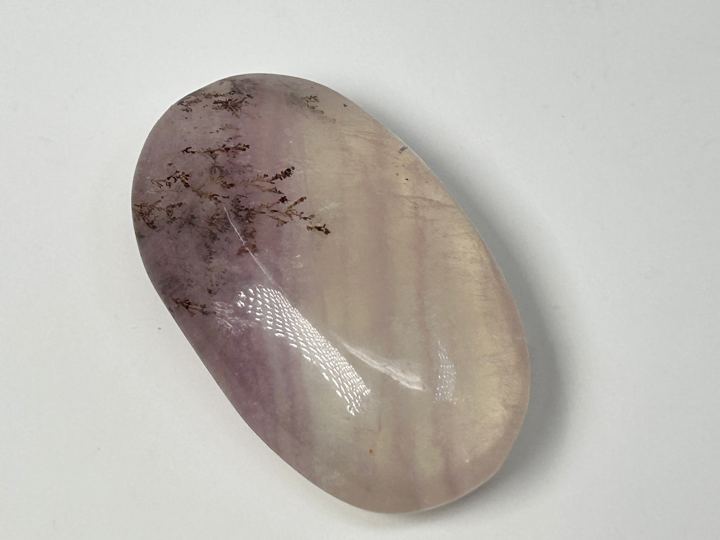Oval-shaped Dendritic Fluorite natural grounding crystal on table with white background.
