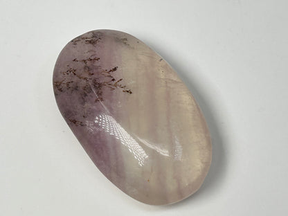 Oval-shaped Dendritic Fluorite natural grounding crystal on table with white background.