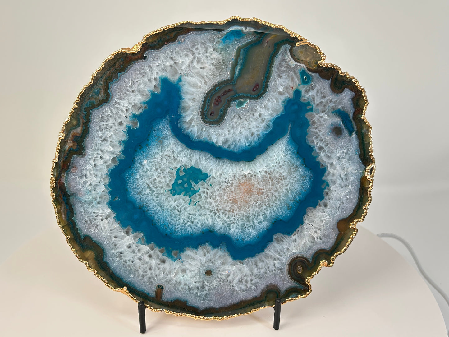 Dyed Blue Agate Plate with gold trim for meditation and energy work on a stand with a white background