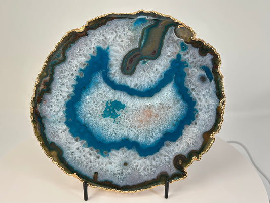 Dyed Blue Agate Plate with gold trim for meditation and energy work on a stand with a white background