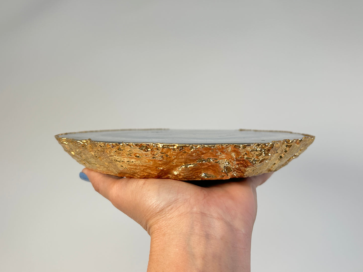 Hand holding a Dyed Blue Agate Plate with gold flake design against a plain background