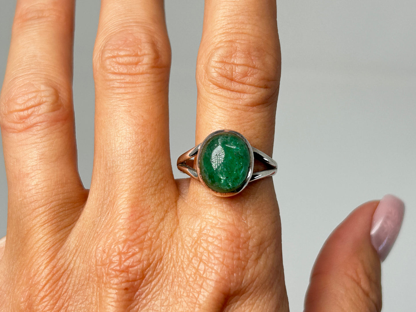 Hand wearing an Emerald Tanzurine Sterling Silver Ring for spiritual healing against white background.